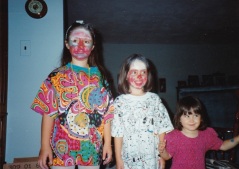 Three sisters standing in height order, the older two having many colors of make up covering every inch of their faces.